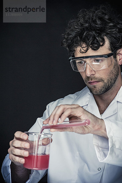 Chemiker gießt Flüssigkeit aus dem Reagenzglas in das Becherglas