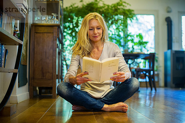 Reife Frau sitzt zu Hause auf dem Boden  liest Buch