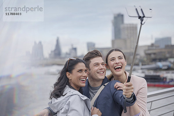Enthusiastische  lächelnde Freund-Touristen  die Selfie mit Selfie-Stick auf urbaner Brücke nehmen  London  UK