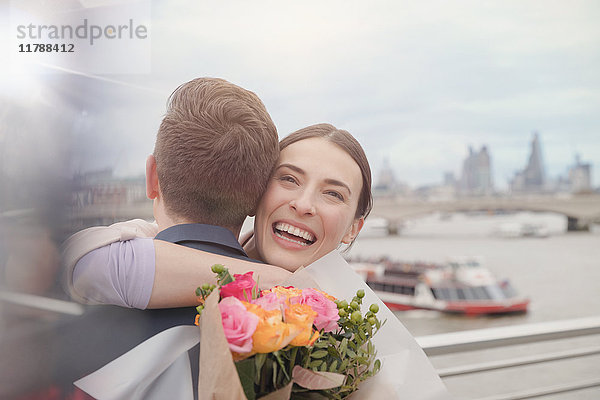 Glückliche  dankbare Frau erhält Blumenstrauß  umarmt Freund am städtischen Ufer