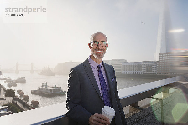 Porträt eines lächelnden  selbstbewussten Geschäftsmannes beim Kaffeetrinken auf der sonnigen Brücke über die Themse  London  UK