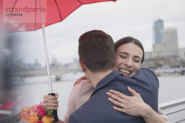 Lächelndes  liebevolles Paar mit Regenschirm und Blumen auf der urbanen Brücke  London  UK