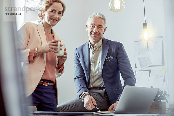 Portrait lächelnde  selbstbewusste Geschäftsleute beim Kaffeetrinken und Arbeiten am Laptop im Büro