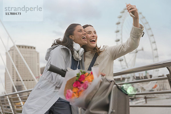 Enthusiastische  lächelnde Frauenfreunde  die Selfie mit Fotohandy in der Nähe von Millennium Wheel  London  UK nehmen