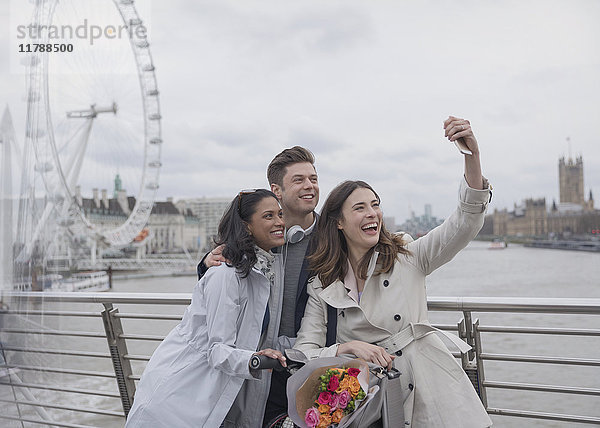Lächelnde  glückliche Freunde nehmen Selfie mit Selfie-Stick auf der Brücke bei Millennium Wheel  London  UK