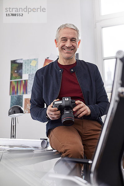 Portrait lächelnder  selbstbewusster Fotograf mit Digitalkamera im Büro