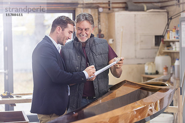 Männliche Kunden unterschreiben Papierkram für fertiges Holzkajak in der Werkstatt