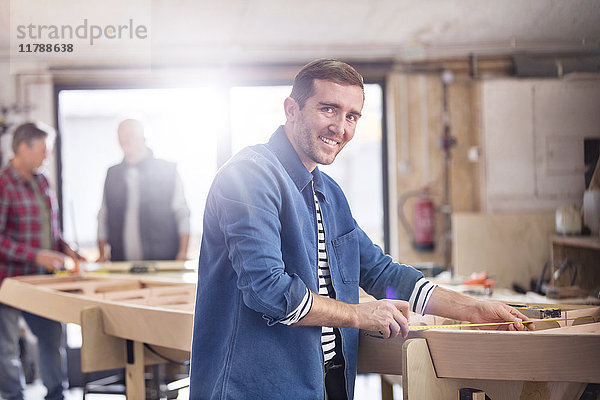 Portrait lächelnder Schreiner beim Messen von Holz auf dem Boot in der Werkstatt