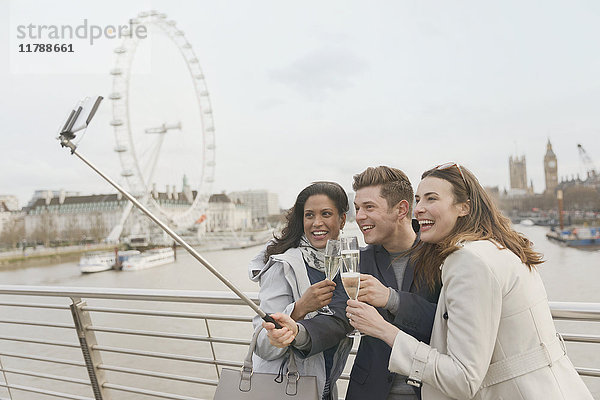 Lächelnde  freundliche Touristen feiern  trinken Champagner und nehmen Selfie mit Selfie Stick in der Nähe von Millennium Wheel  London  UK.