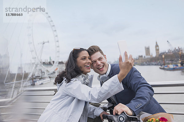 Lächelndes Paar Touristen  die Selfie mit Fotohandy auf der Brücke in der Nähe von Millennium Wheel  London  UK nehmen