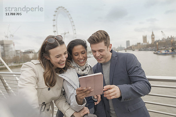 Freundliche Touristen  die ein digitales Tablett auf der Brücke über die Themse benutzen  London  UK