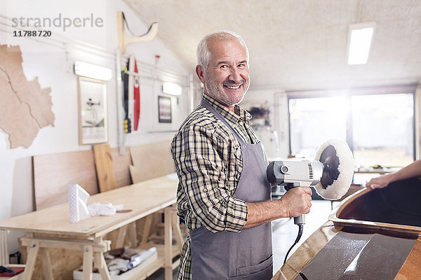 Portrait lächelnder  selbstbewusster Senior-Schreiner mit Pufferschleifer auf Holzboot in der Werkstatt