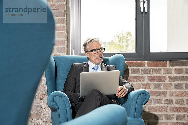 Erwachsener Geschäftsmann im Sessel sitzend  mit Laptop