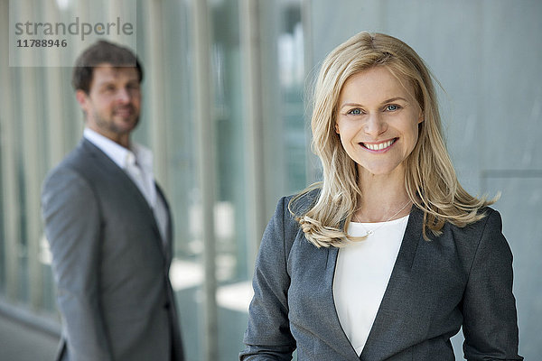 Porträt einer lächelnden Geschäftsfrau mit ihrem Partner im Hintergrund