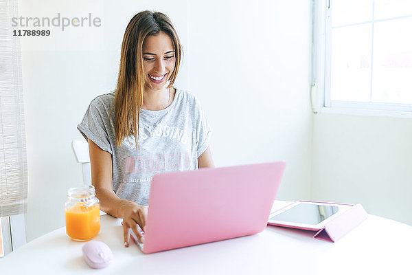 Lächelnde junge Frau bei der Arbeit mit Laptop und Tablett zu Hause