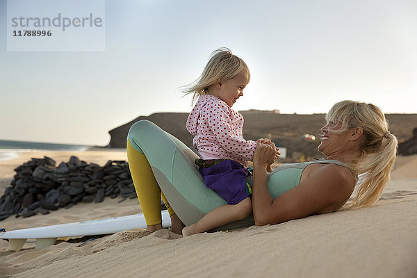 Spanien  Fuerteventura  glückliche Mutter und Tochter am Strand neben dem Surfbrett bei Sonnenuntergang