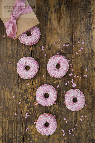 Doughnuts mit rosa Glasur und Zuckergranulat und Backdekor auf Holz