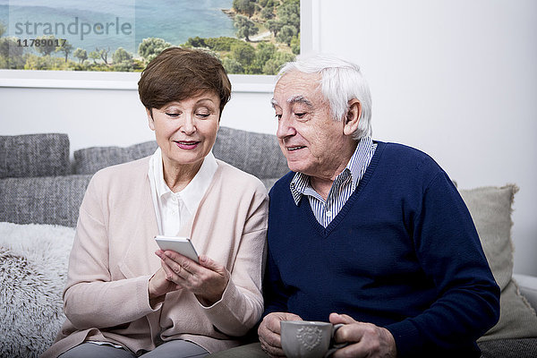 Seniorenpaar auf der Couch liegend mit Smartphone