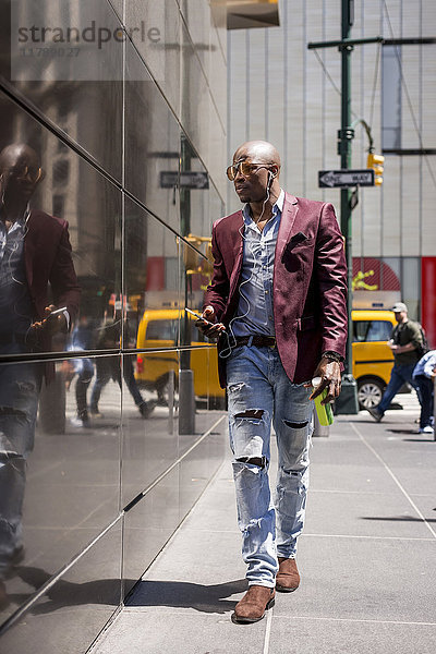 USA  New York City  Manhattan  stilvoller Geschäftsmann beim Musikhören mit Kopfhörer und Smartphone