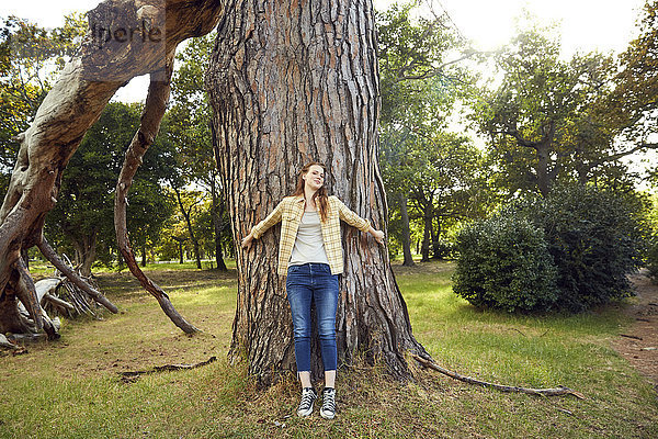 Lächelnde junge Frau an Baumstamm gelehnt