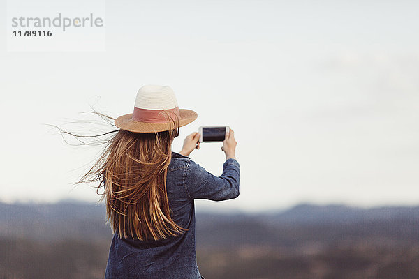 Rückansicht der rothaarigen Frau beim Fotografieren mit dem Smartphone in der Natur
