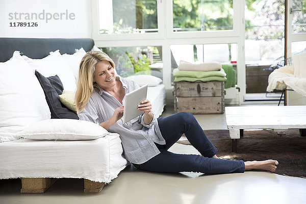 Entspannte Frau sitzend auf dem Boden des Wohnzimmers mit Tablette