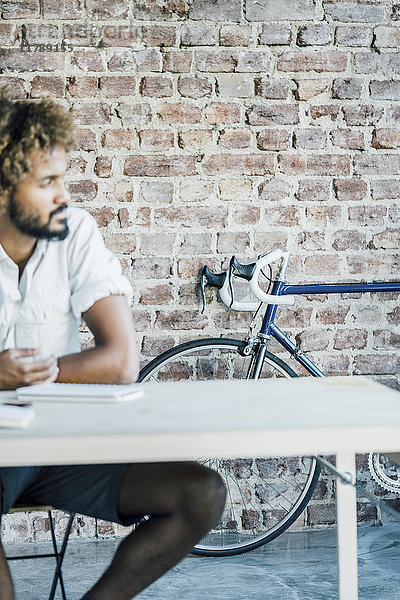 Junger Mann am Schreibtisch denkt mit Fahrrad im Hintergrund