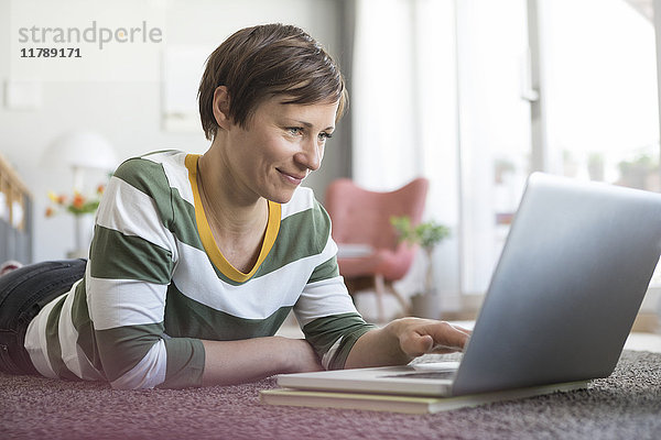 Lächelnde Frau zu Hause auf dem Boden liegend mit Laptop