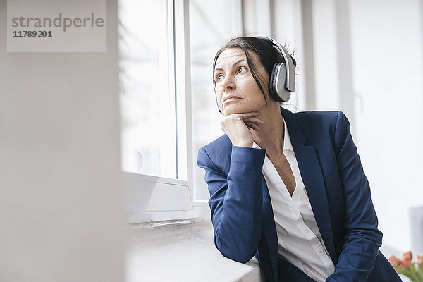Porträt einer Frau  die aus dem Fenster schaut  während sie über Kopfhörer Musik hört.