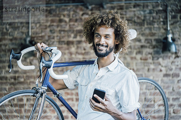 Lächelnder junger Mann mit Fahrrad und Handy