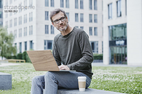Erwachsener Mann im Freien mit Laptop und Kaffee zum Mitnehmen