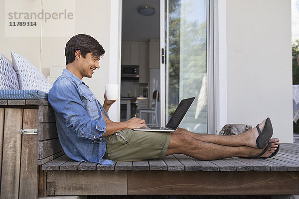 Mann sitzt auf der Terrasse mit Laptop
