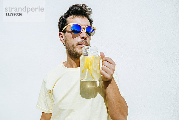 Mann mit Sonnenbrille trinkt Limonade in der weißen Vorderwand