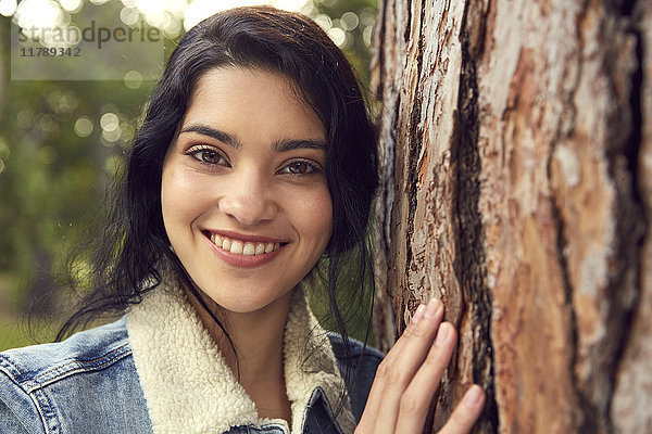 Porträt der lächelnden jungen Frau neben dem Baumstamm