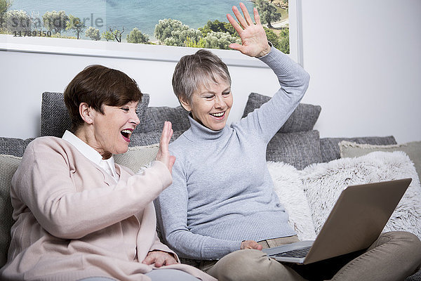Zwei ältere Frauen sitzen auf der Couch und beobachten den Laptop.