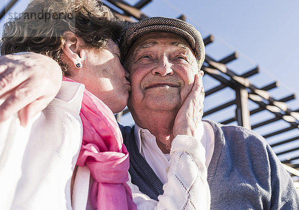 Porträt eines glücklichen älteren Mannes  der von seiner Frau geküsst wurde.