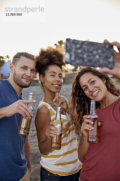 Drei Freunde mit Bierflaschen  die Selfie am Strand mitnehmen.