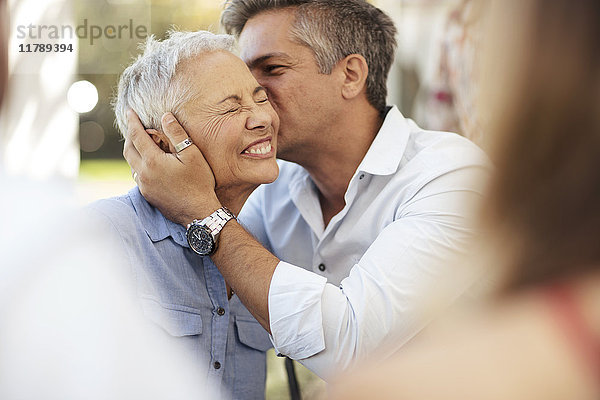 Erwachsener Sohn küsst glückliche Seniorin im Freien