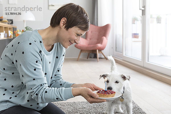 Lächelnde Frau präsentiert ihrem Hund einen Geburtstagskuchen