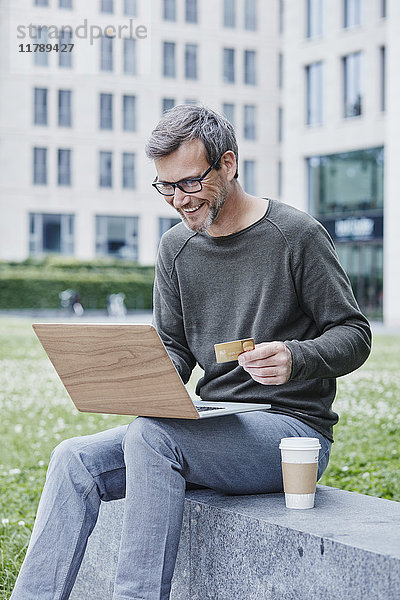 Erwachsener Mann im Freien mit Laptop  Kreditkarte und Kaffee zum Mitnehmen