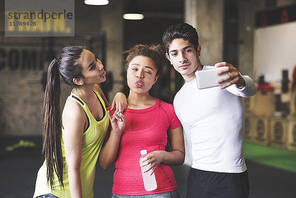Drei verspielte junge Leute  die einen Selfie im Fitnessstudio nehmen.