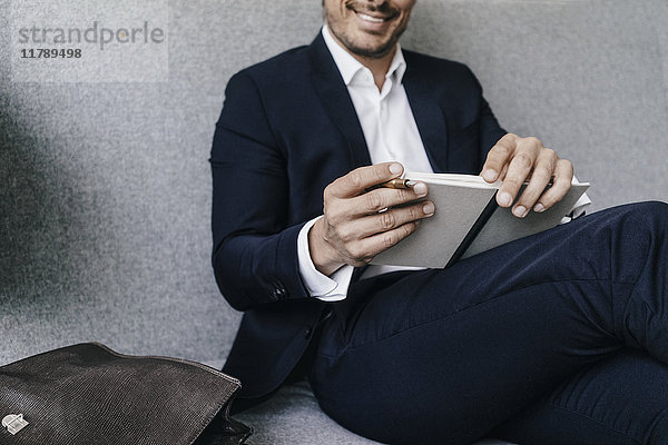 Lächelnder Geschäftsmann mit Notizbuch auf der Couch