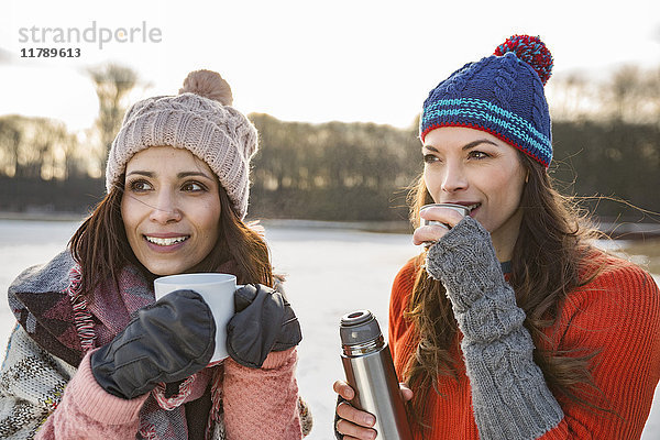 Zwei Frauen trinken im Winter heiße Getränke im Freien.