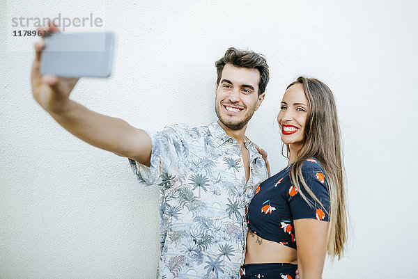 Paar  das einen Selfie mit Smartphone vor der weißen Wand nimmt