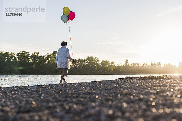 Rückansicht einer älteren Frau mit Luftballons am Ufer des Flusses