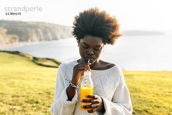 Junge Frau trinkt Orangensaft an der Küste