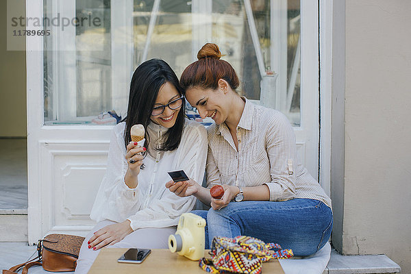 Zwei glückliche Freunde mit Eiscreme beim Fotografieren in der Stadt