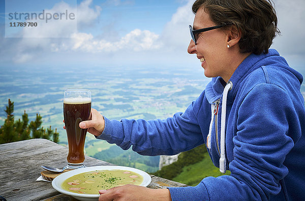 Deutschland  Chiemgau  fröhlicher Wanderer auf Hochfelln mit Bier und Erbsensuppe