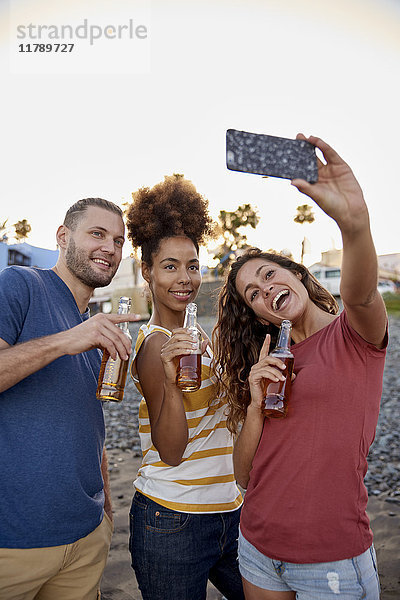 Drei Freunde mit Bierflaschen  die Selfie am Strand mitnehmen.