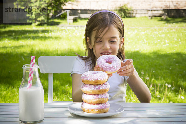 Mädchen mit Donuts auf Gartentisch